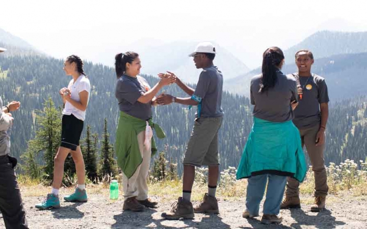 a group of outward bound students stand on an overlook while two play patty cake with their hands